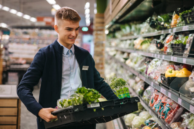 Shop assistant in supermarket re-stocking fresh vegetables