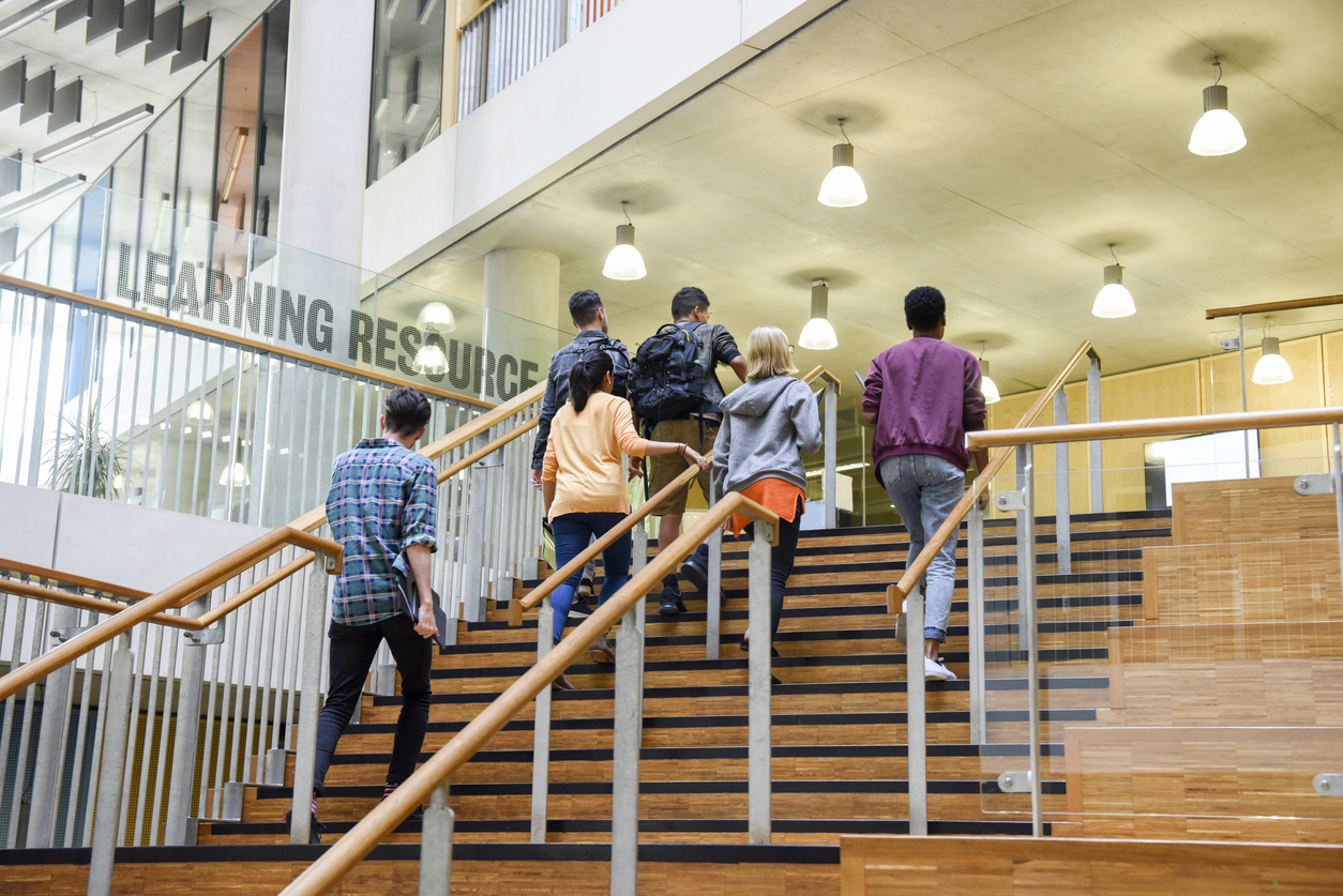 Six students walking up wooden steps in modern college building