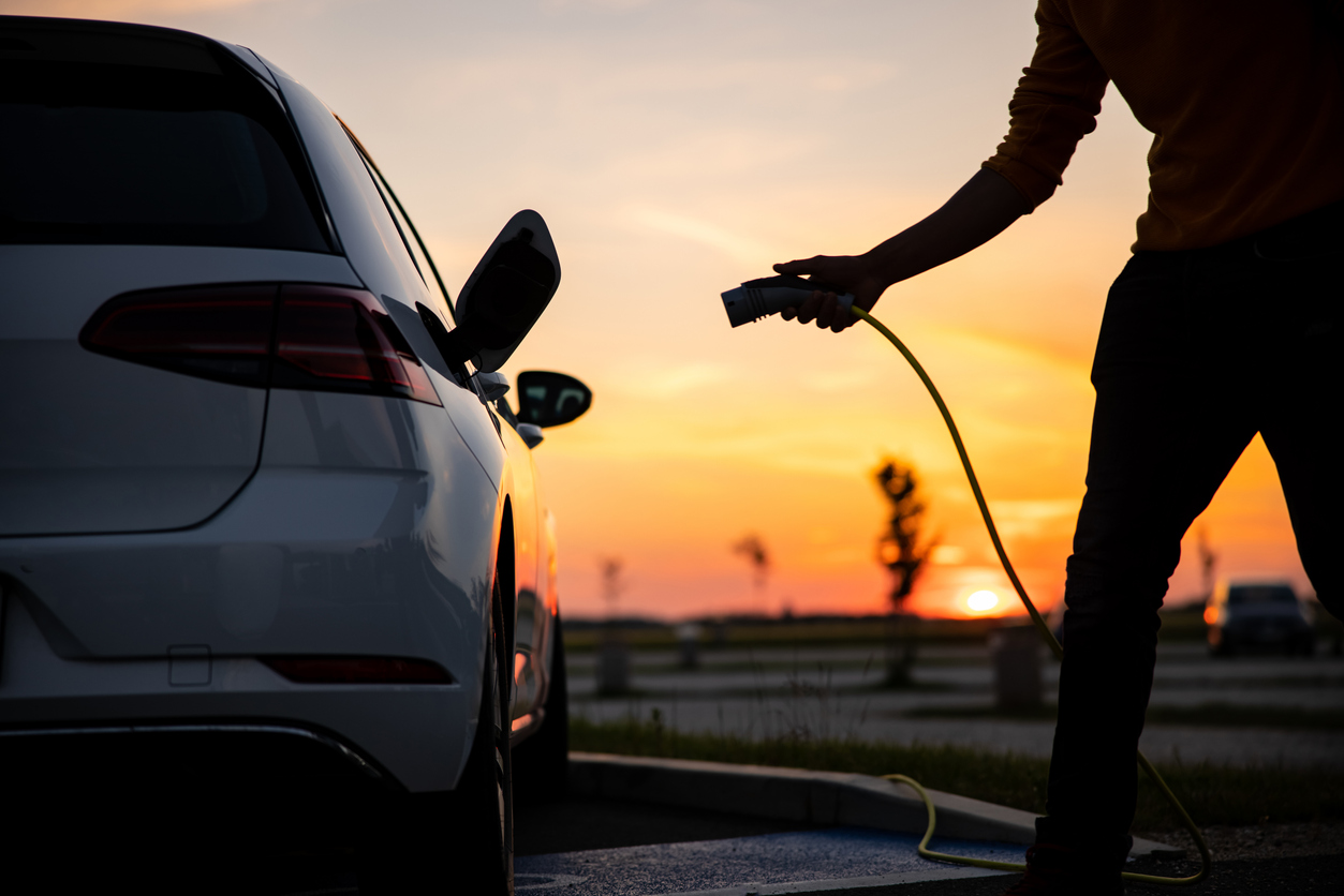 Silhouette of man inserting plug into the electric car charging socket