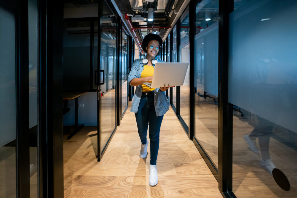 Happy African American IT technician working late at the office using her laptop and smiling