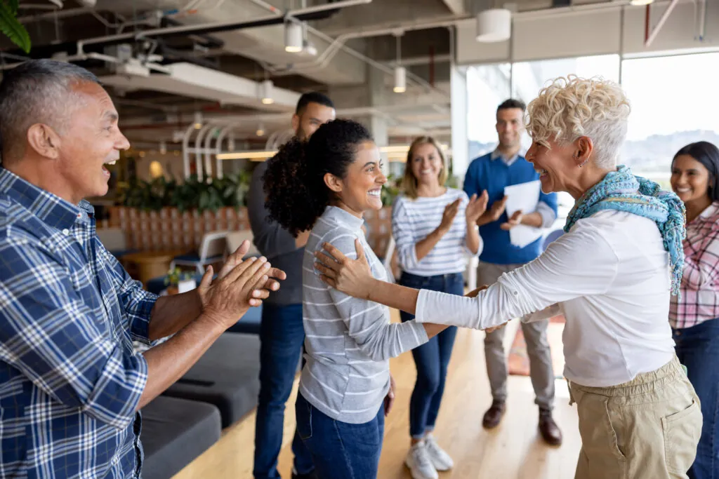 Boss giving woman a promotion at the office and team clapping for her in a business meeting